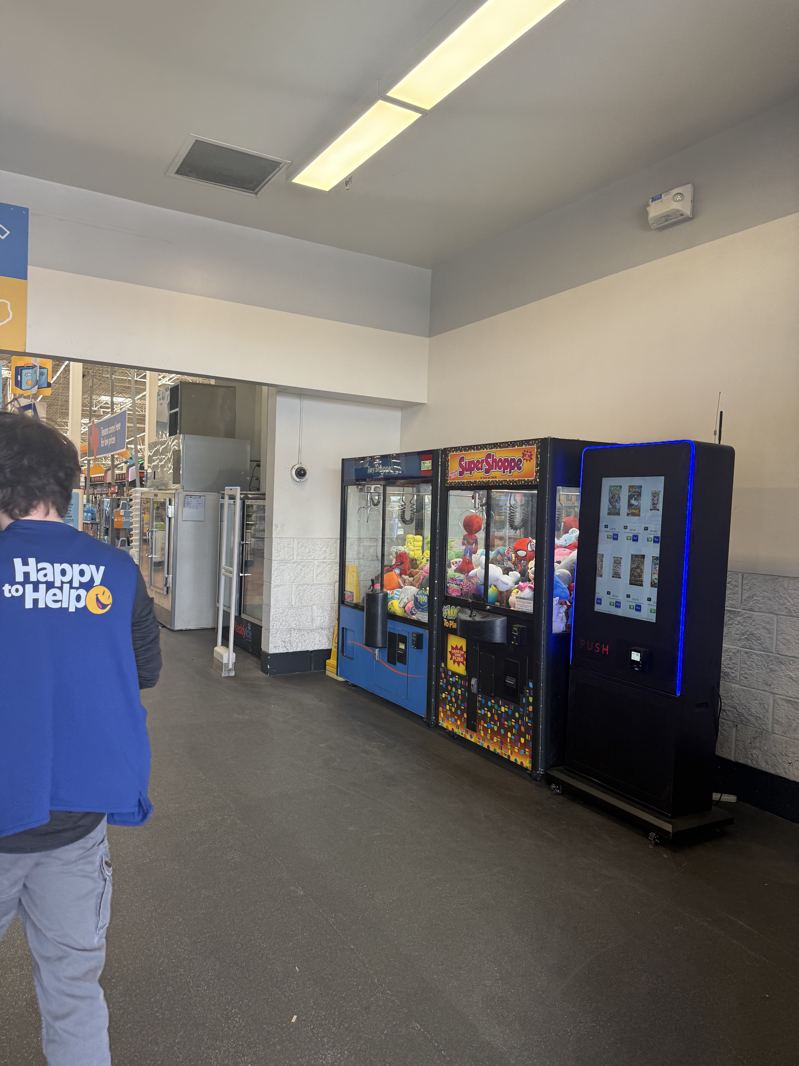 Black kiosk beside two claw machines in a store vestibule